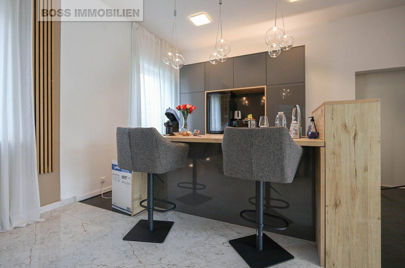 Moderne Teeküche mit Barhockern, Hängeschränken und stilvollen Pendelleuchten.