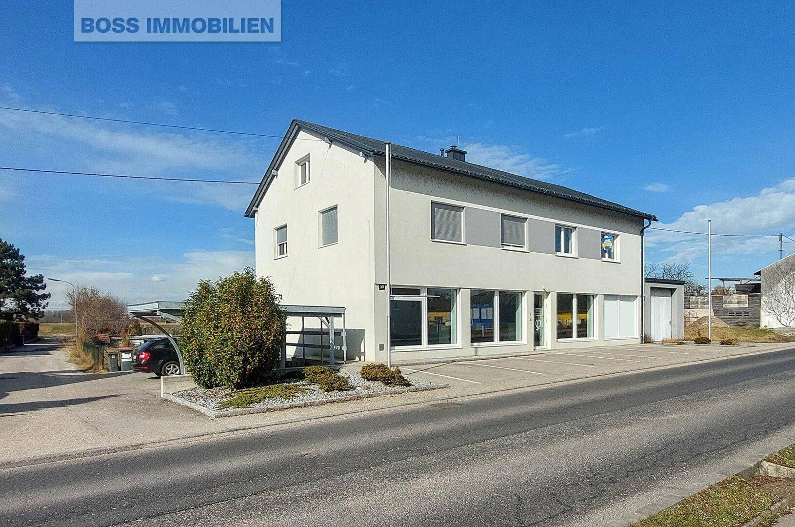 Modernes Geschäftsgebäude mit großen Fenstern, Parkplätzen und einem Carport auf dem Grundstück.