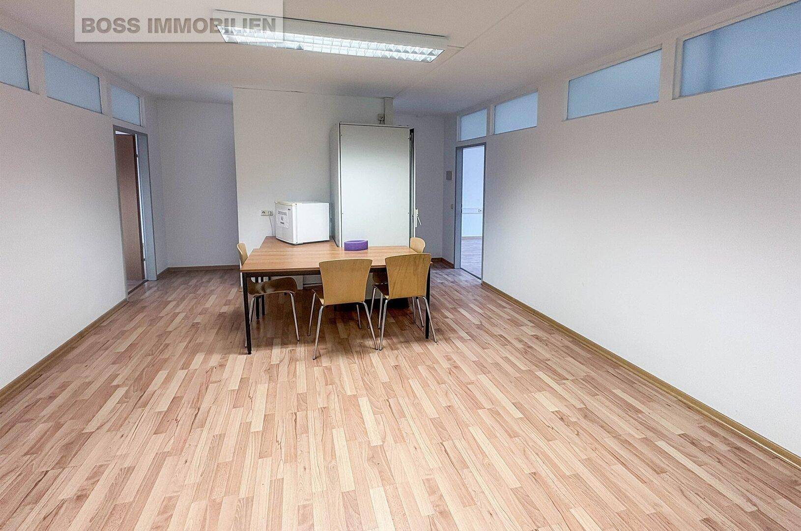 Gemeinschaftsbüro oder Besprechungsraum mit Holzboden, Tisch und Stühlen, sowie Oberlichtern.