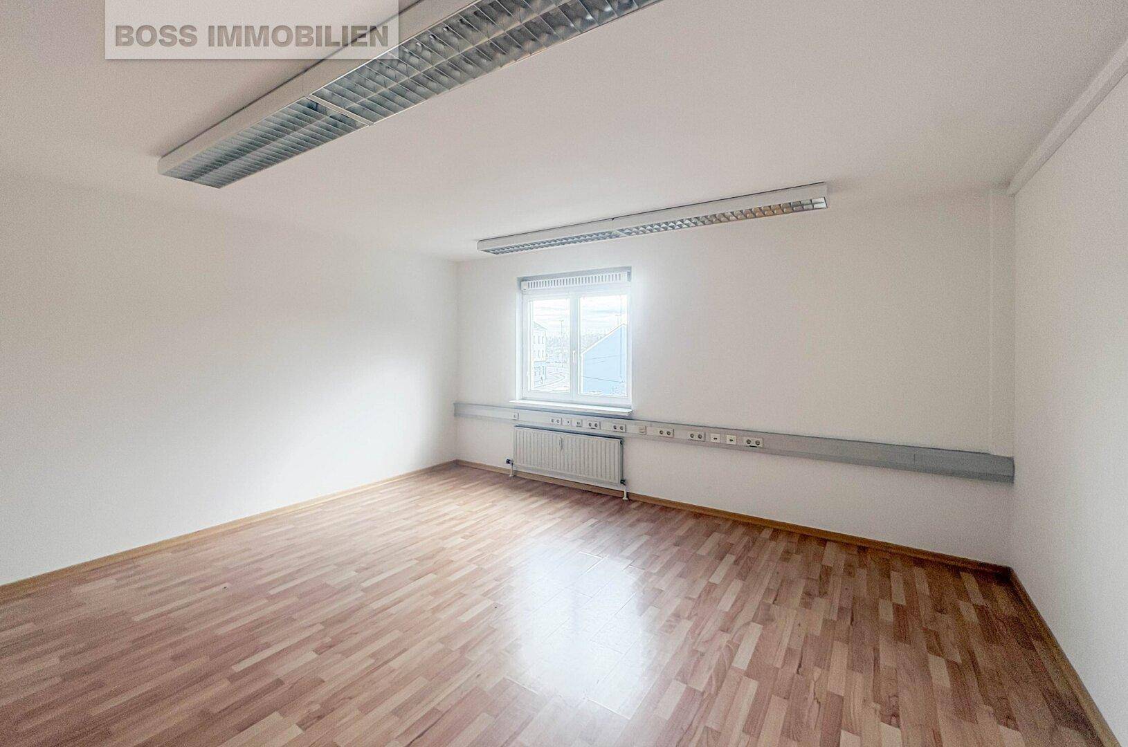 Leeres Büro mit weiß gestrichenen Wänden und Holzparkett, bereit zur individuellen Gestaltung.