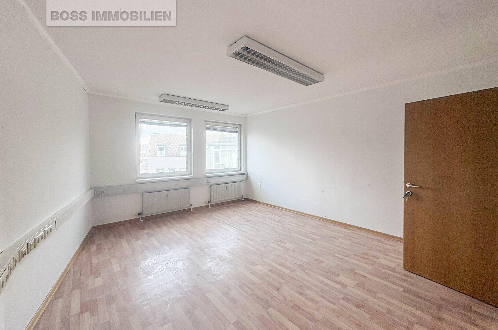 Heller Büroraum mit zwei Fenstern, Holzfußboden und weißen Wänden, ideal für produktives Arbeiten.