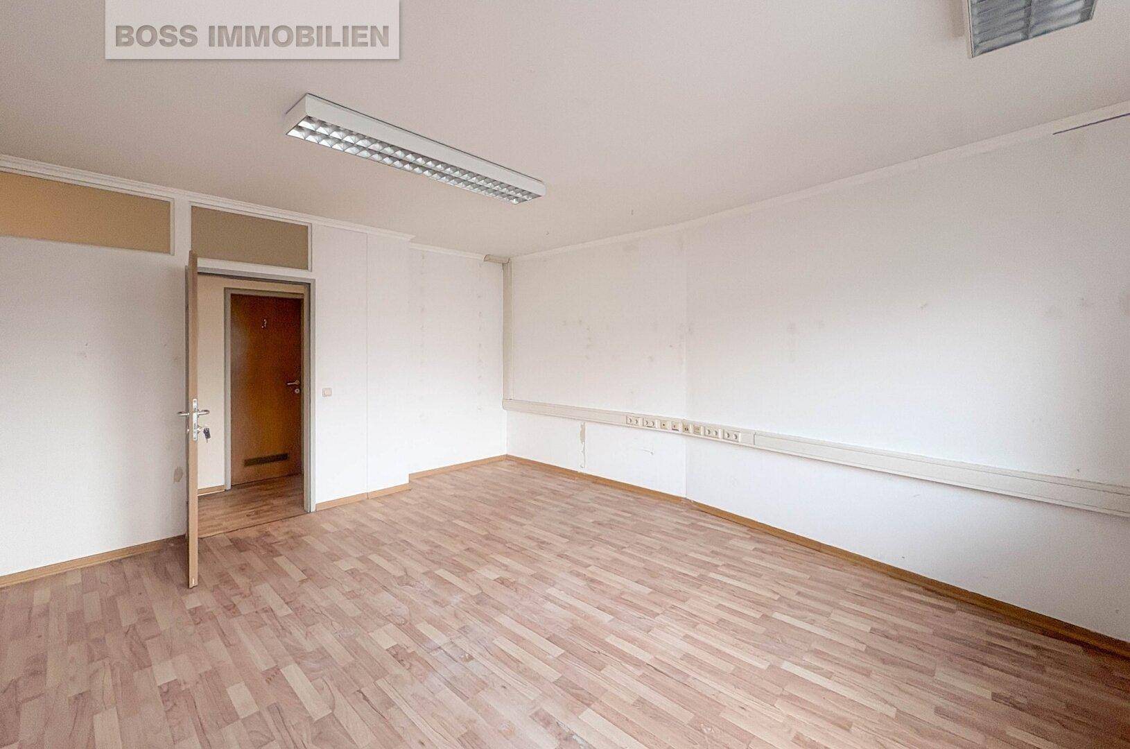 Unmöblierter Büroraum mit Holzboden und Zugang zu weiteren Bereichen, ideal für flexible Nutzung.