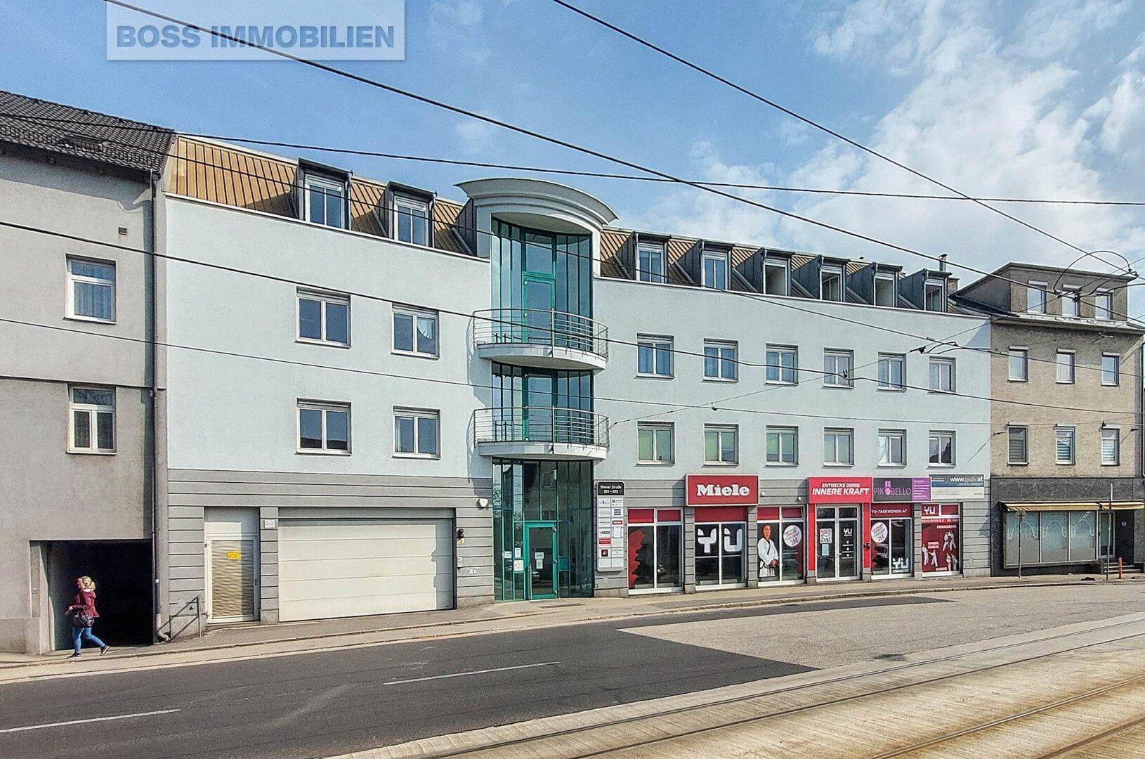 Mehrstöckiges Geschäfts- und Wohngebäude mit moderner Glasfassade und Ladenflächen im Erdgeschoss.