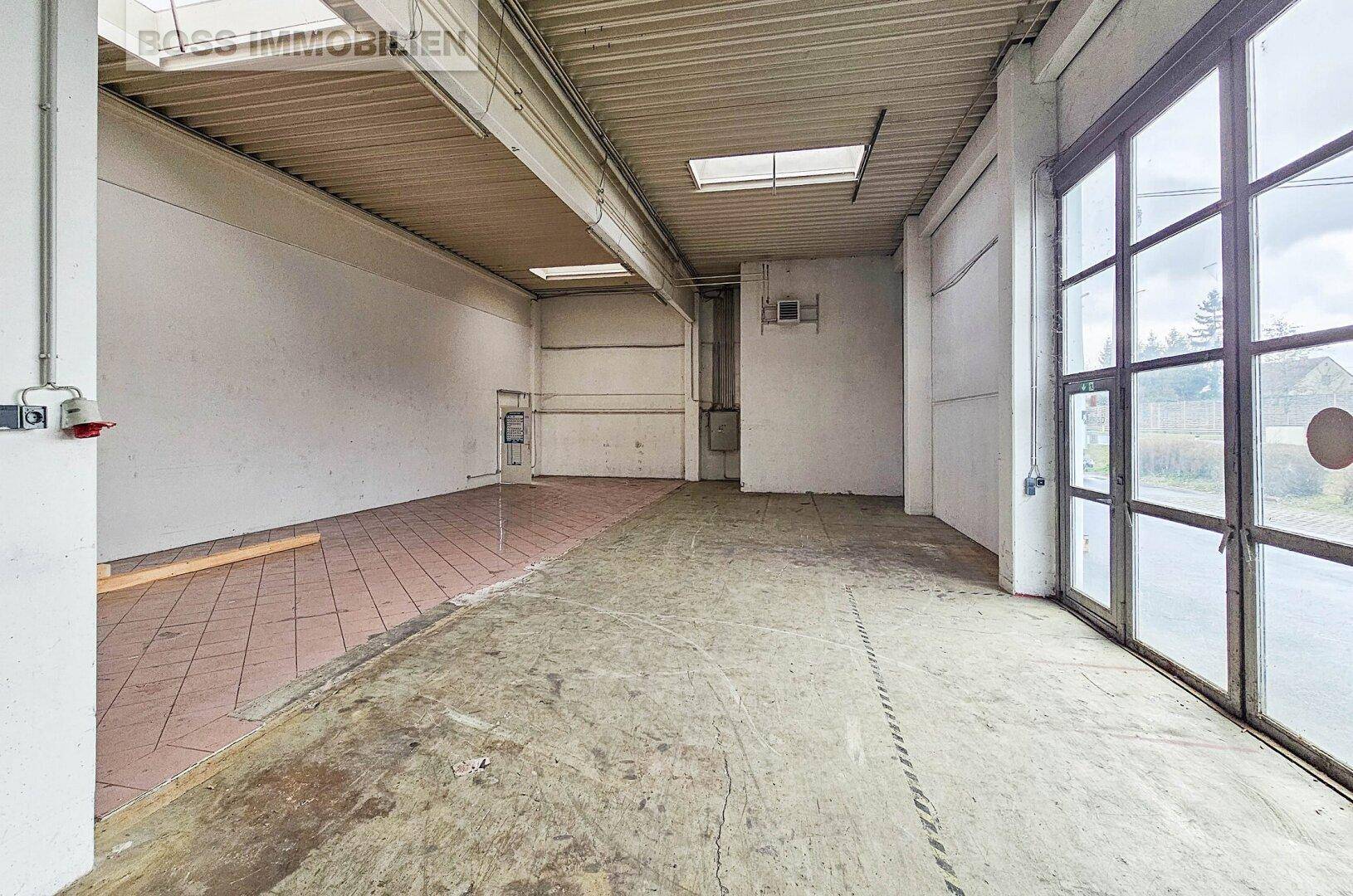 Heller Gewerberaum mit Betonboden, großen Fenstern und hohen Decken.