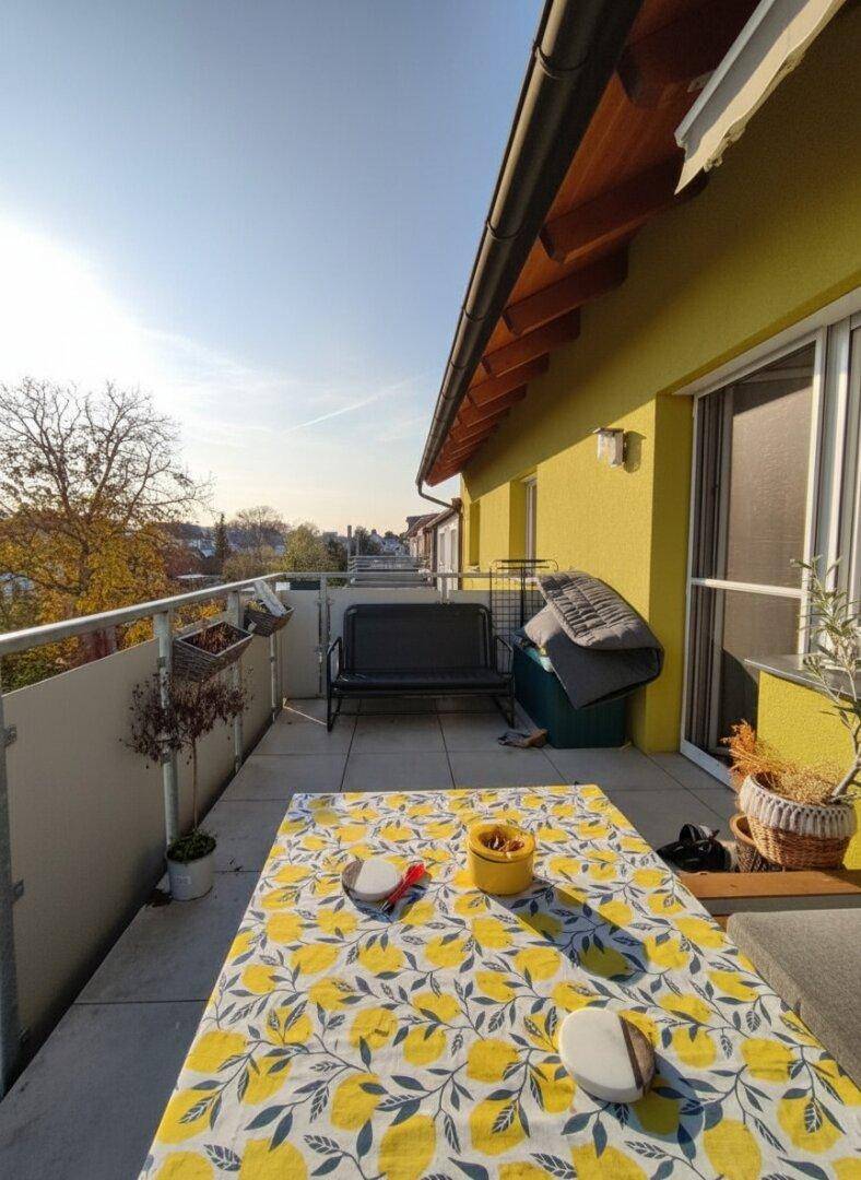 Sonniger Balkon mit Esstisch, Sitzbank und weitem Blick über die Dächer.