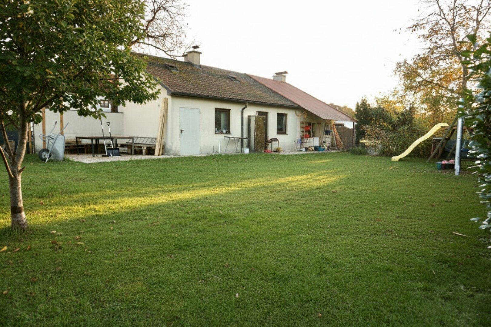 Großer, gepflegter Garten hinter dem Haus mit Rasenfläche, Bäumen und Kinderspielgeräten.