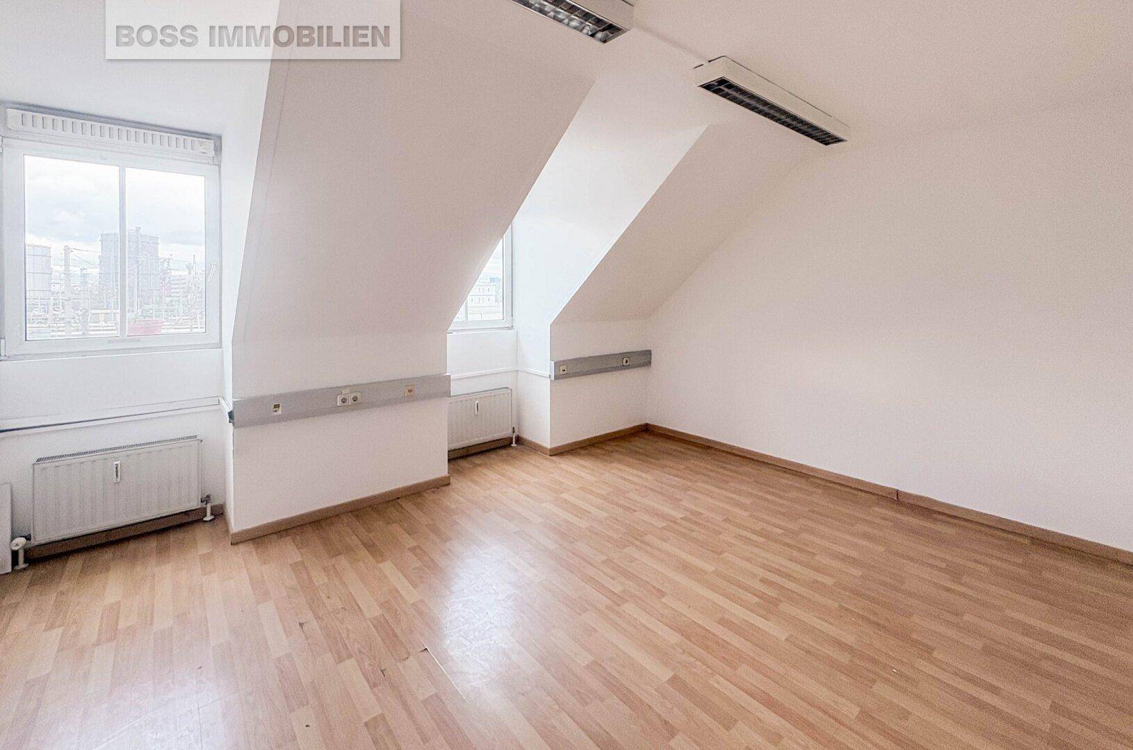 Geräumiger Büroraum im Dachgeschoss mit zwei Fenstern, Schrägen und einem hellen Laminatboden.