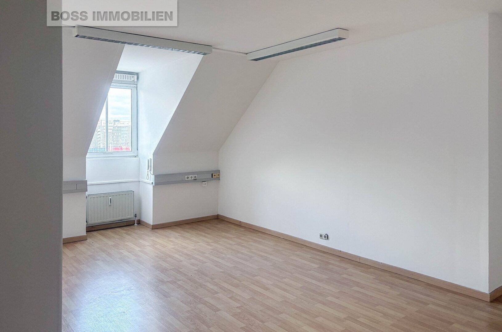 Heller Büroraum im Dachgeschoss mit Schrägen, Laminatboden und einem Fenster, das viel Tageslicht hereinlässt.
