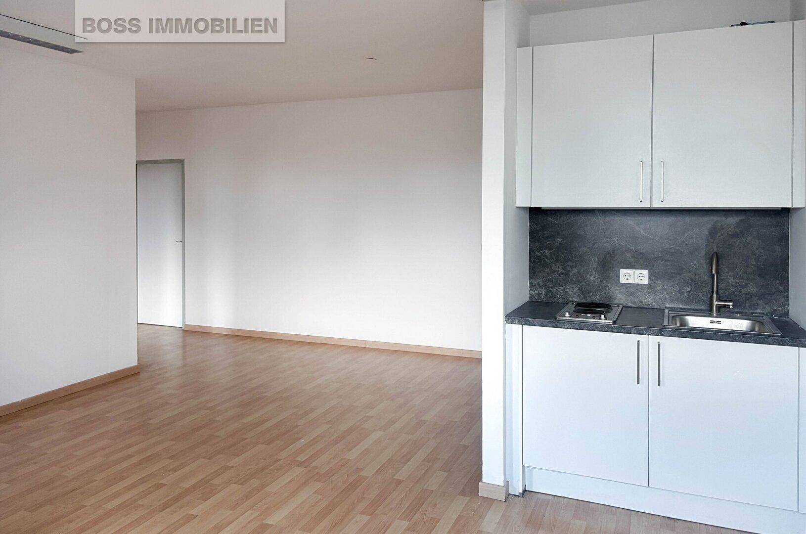 Heller Raum mit einer kompakten, modernen Küchenzeile, Laminatboden und weißen Wänden.