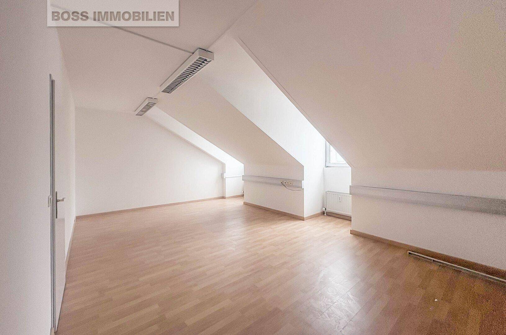 Großer, heller Büroraum mit Dachschrägen, Laminatboden und weiß gestrichenen Wänden, bereit zum Bezug.