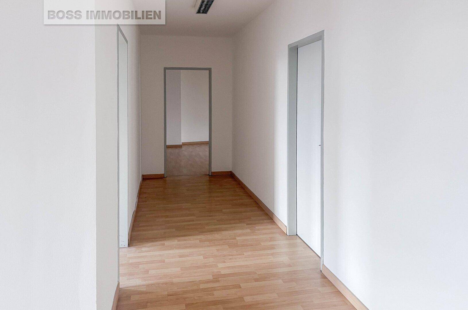 Langer, heller Flur mit Laminatboden und mehreren Türen, die zu verschiedenen Räumen führen.