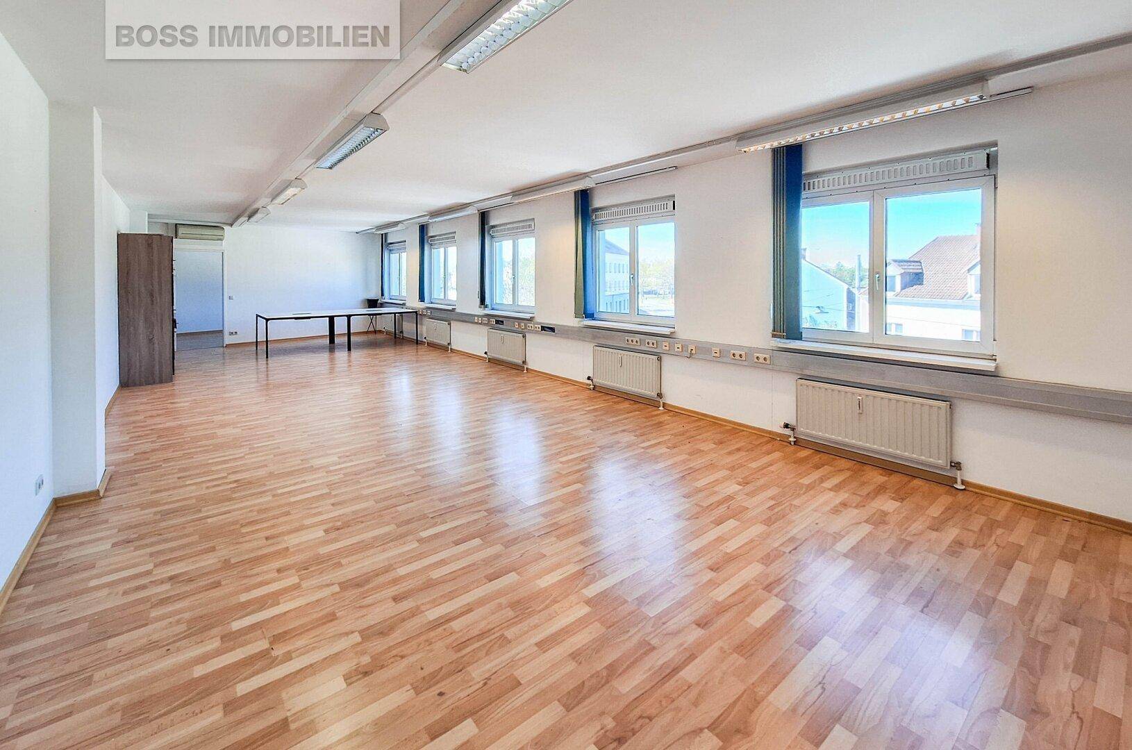 Helles und geräumiges Büro mit Laminatboden und mehreren Fenstern, ideal für verschiedene Nutzungen.