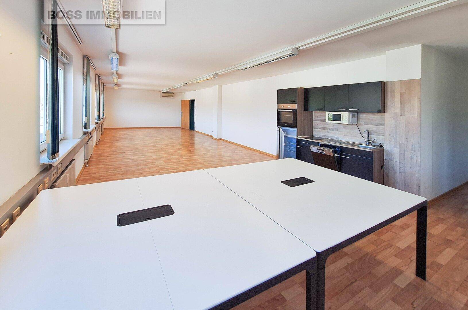 Großes Büro mit integrierter Küchenzeile und modernen Arbeitstischen, ideal für Teamarbeit.