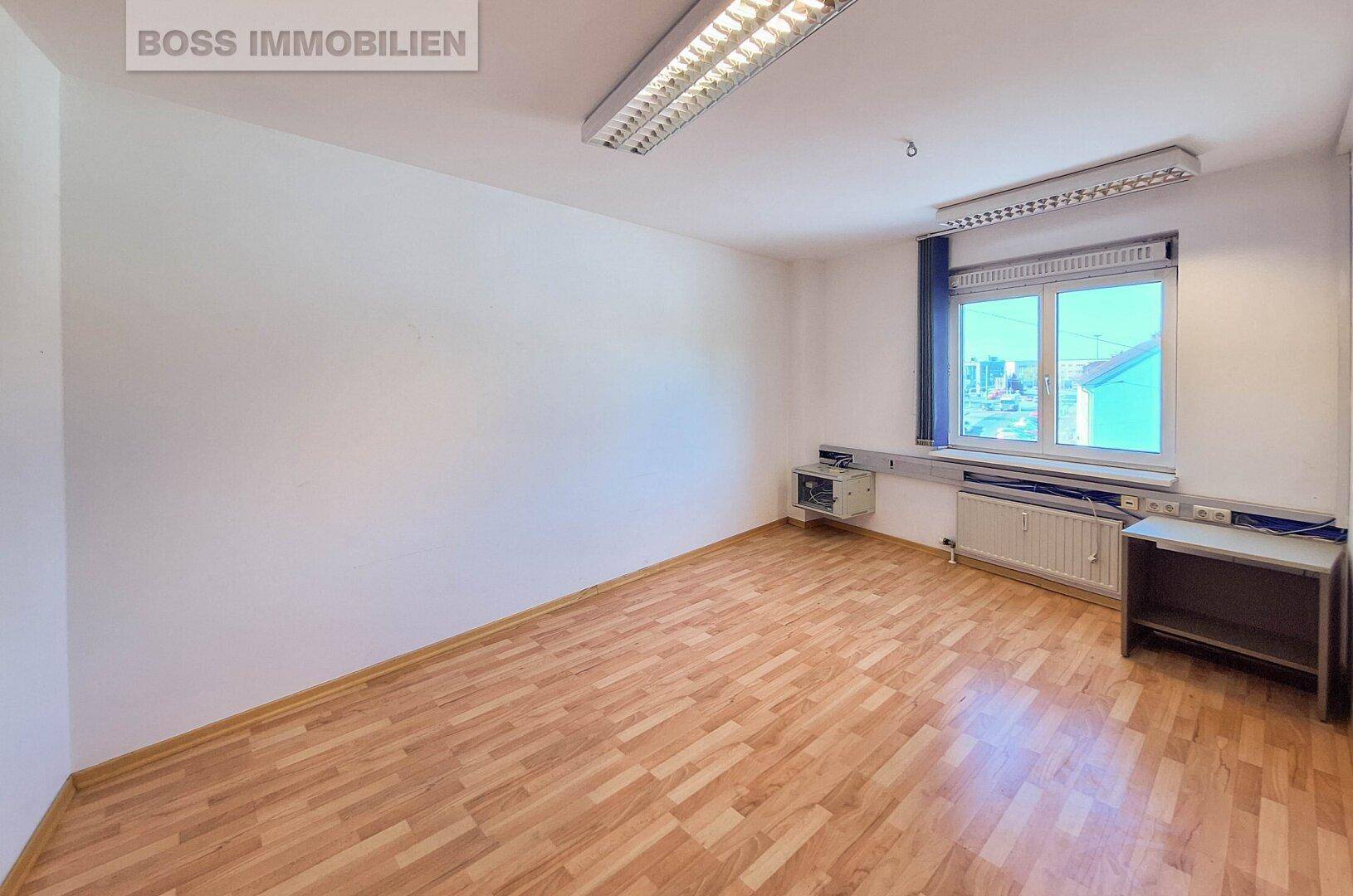 Kleineres, helles Büro mit Laminatboden, Fenster und Wandinstallationen für Arbeitsgeräte.