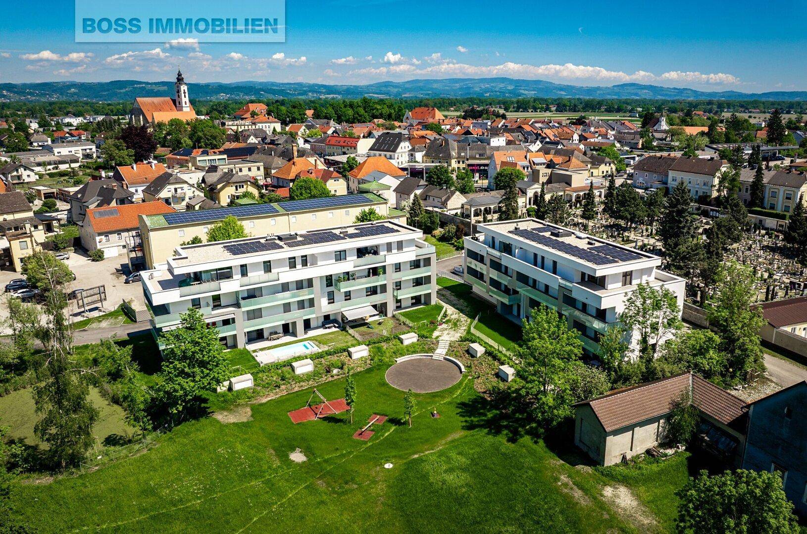 Luftaufnahme einer modernen Wohnanlage mit Grünflächen, Spielplatz und Gemeinschaftspool in ländlicher Umgebung.