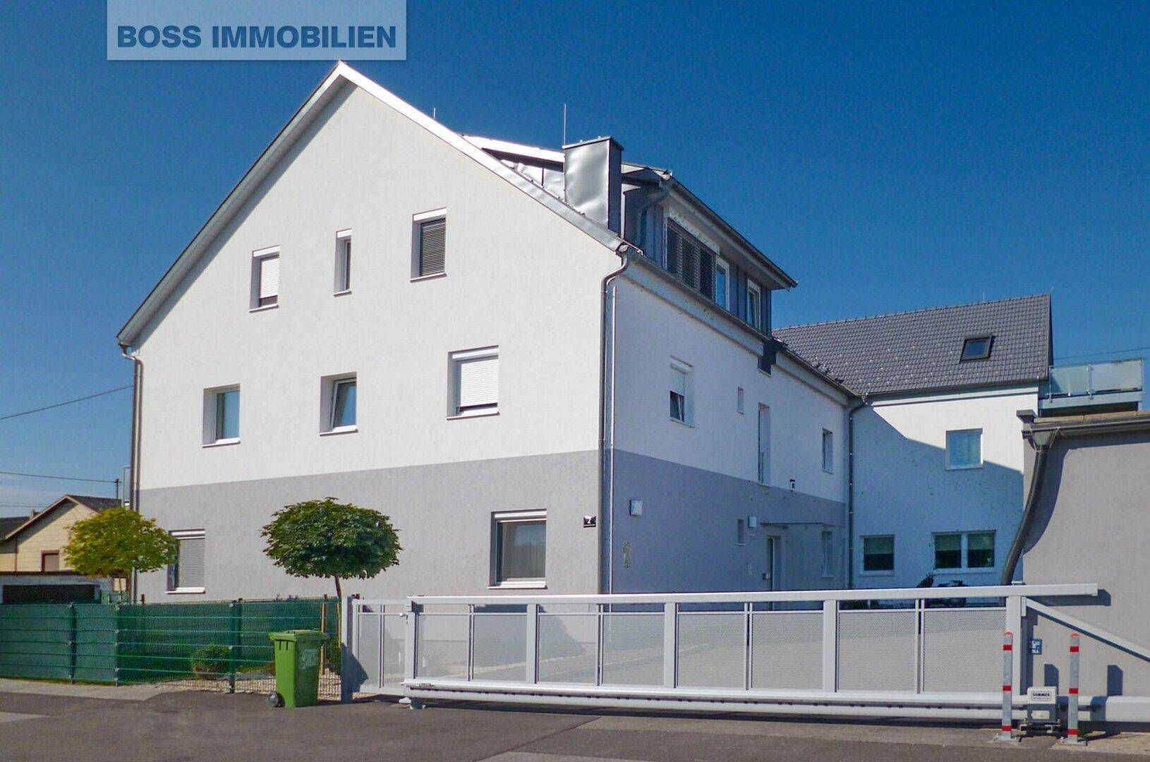 Rückansicht eines modernen Wohnhauses mit Satteldach, Balkonen und Schiebetor zur Einfahrt.