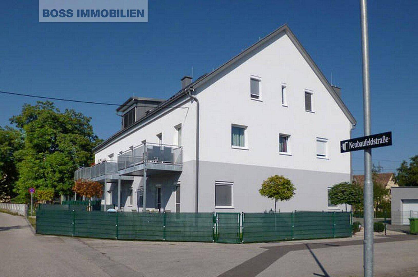 Wohngebäude mit moderner Architektur, Balkonen und einer grünen Hecke an der Neubaufeldstraße.
