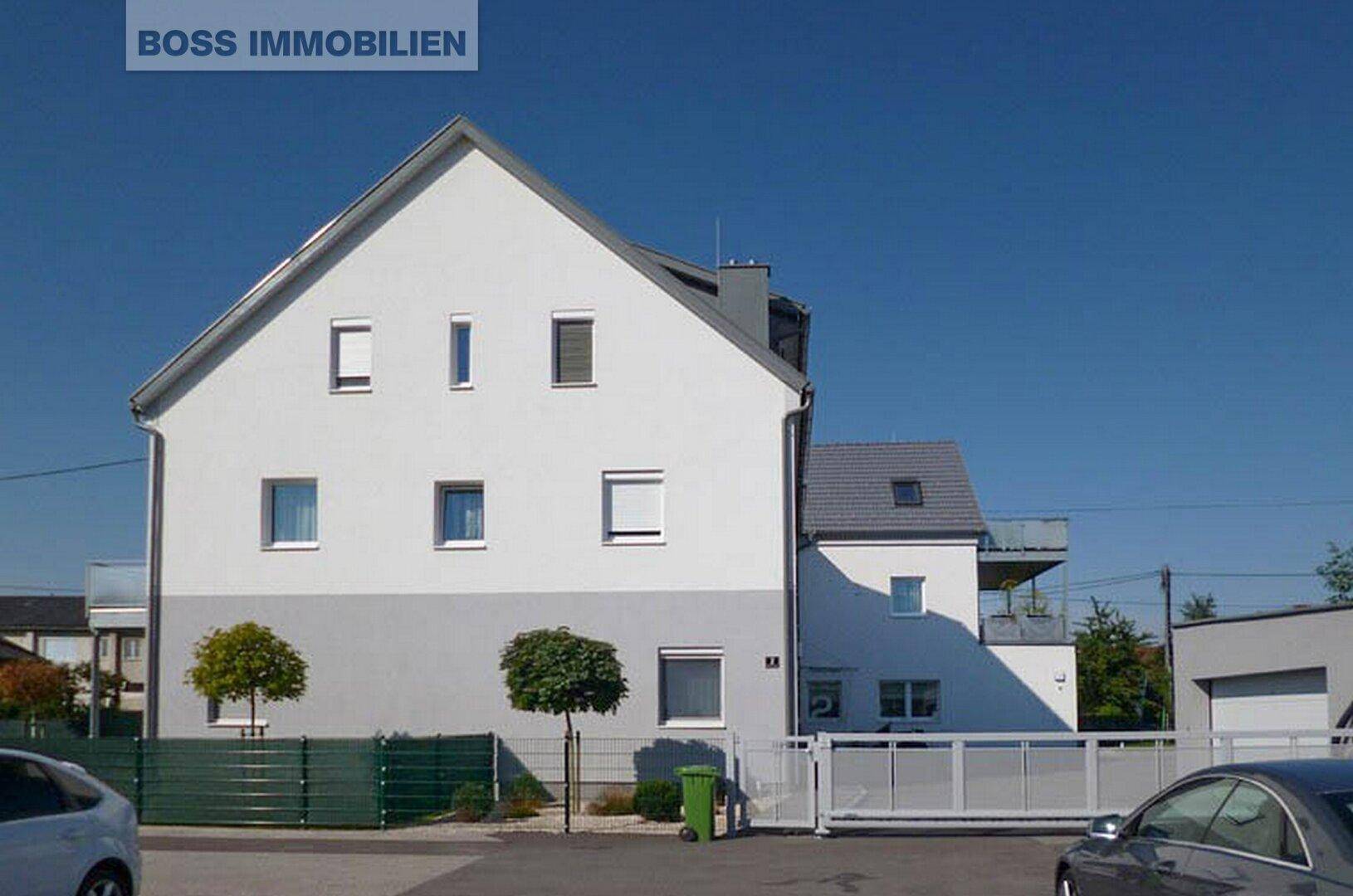 Seitenansicht eines modernen Wohnhauses mit weißer Fassade, Satteldach und Schiebetor zur Einfahrt.