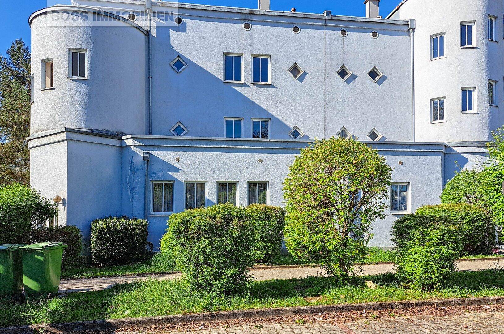 Ansicht des modernen Gebäudes mit hellblauer Fassade, runden Elementen und gepflegter Grünanlage.