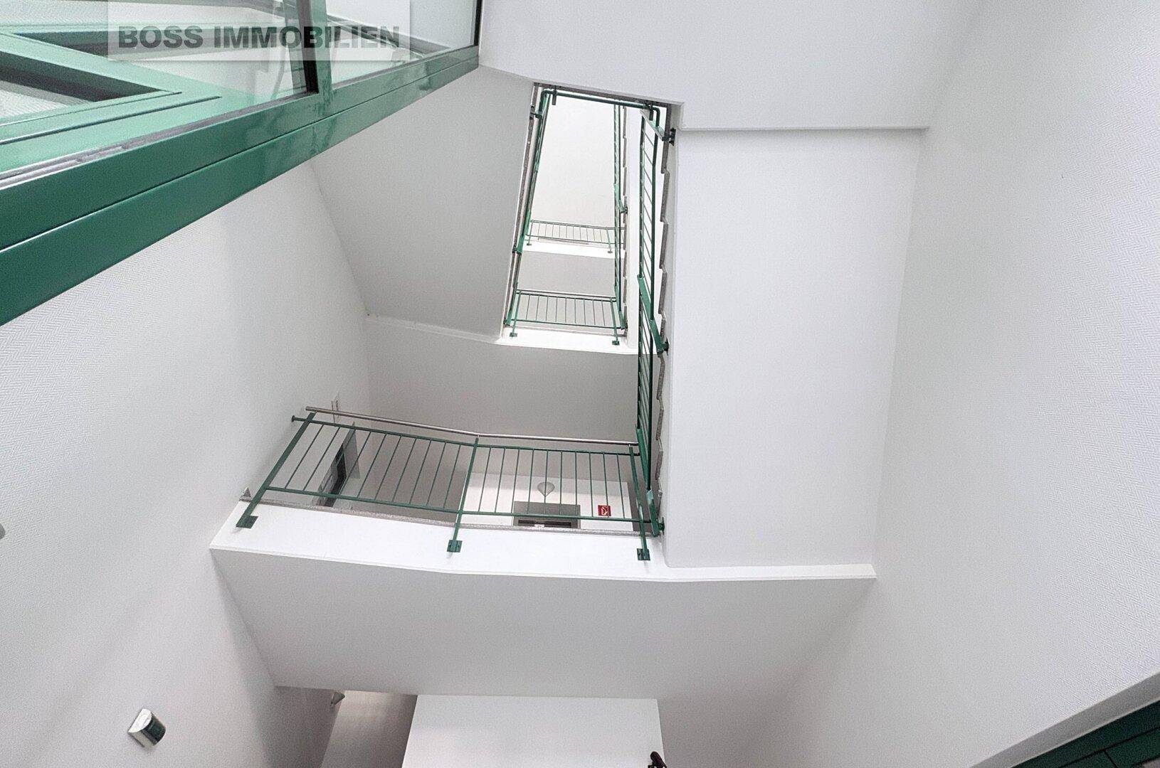 Modernes Treppenhaus mit grünen Geländern und viel Tageslicht von oben.