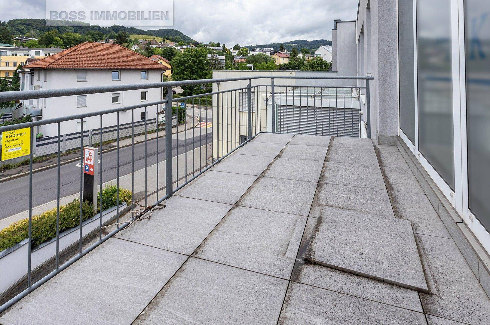 Geräumiger Balkon mit Fliesenboden und Blick auf die Straße und umliegende Hügel.