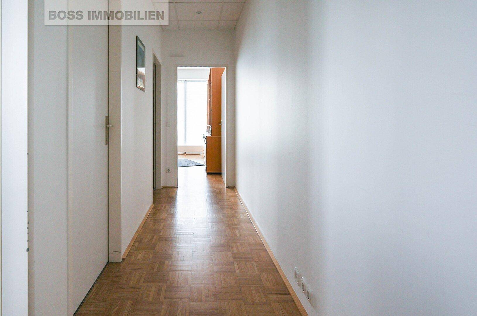 Heller Flur mit Parkettboden und weißen Wänden, der zu weiteren Räumen führt.