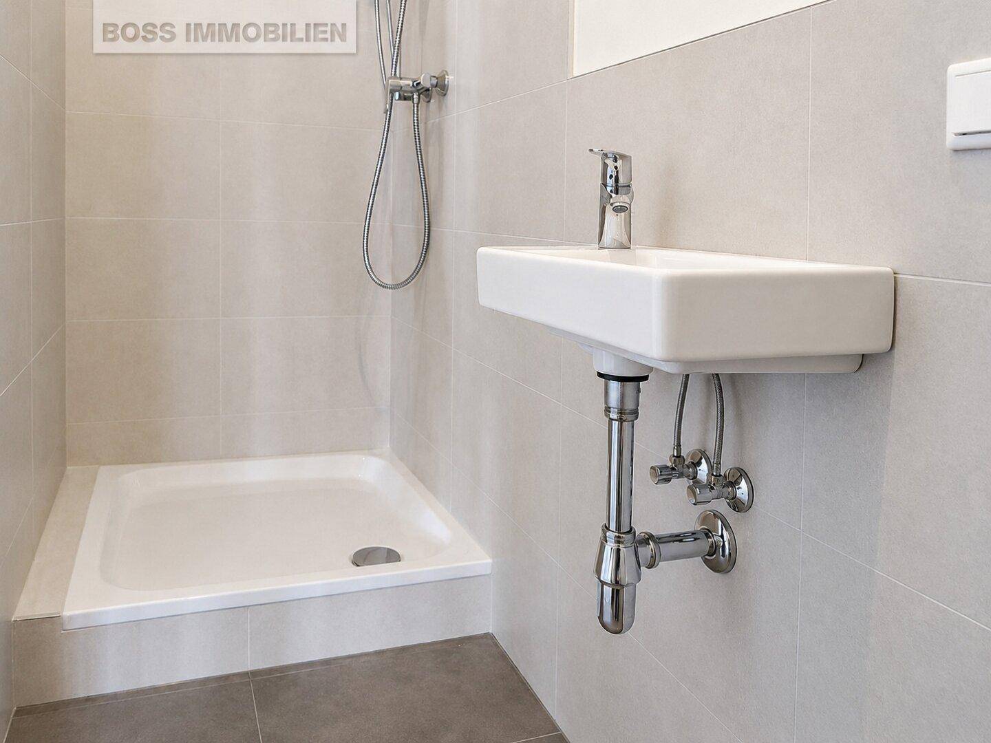 Modernes Badezimmer mit ebenerdiger Dusche und einem wandmontierten Waschbecken in hellen Grautönen.