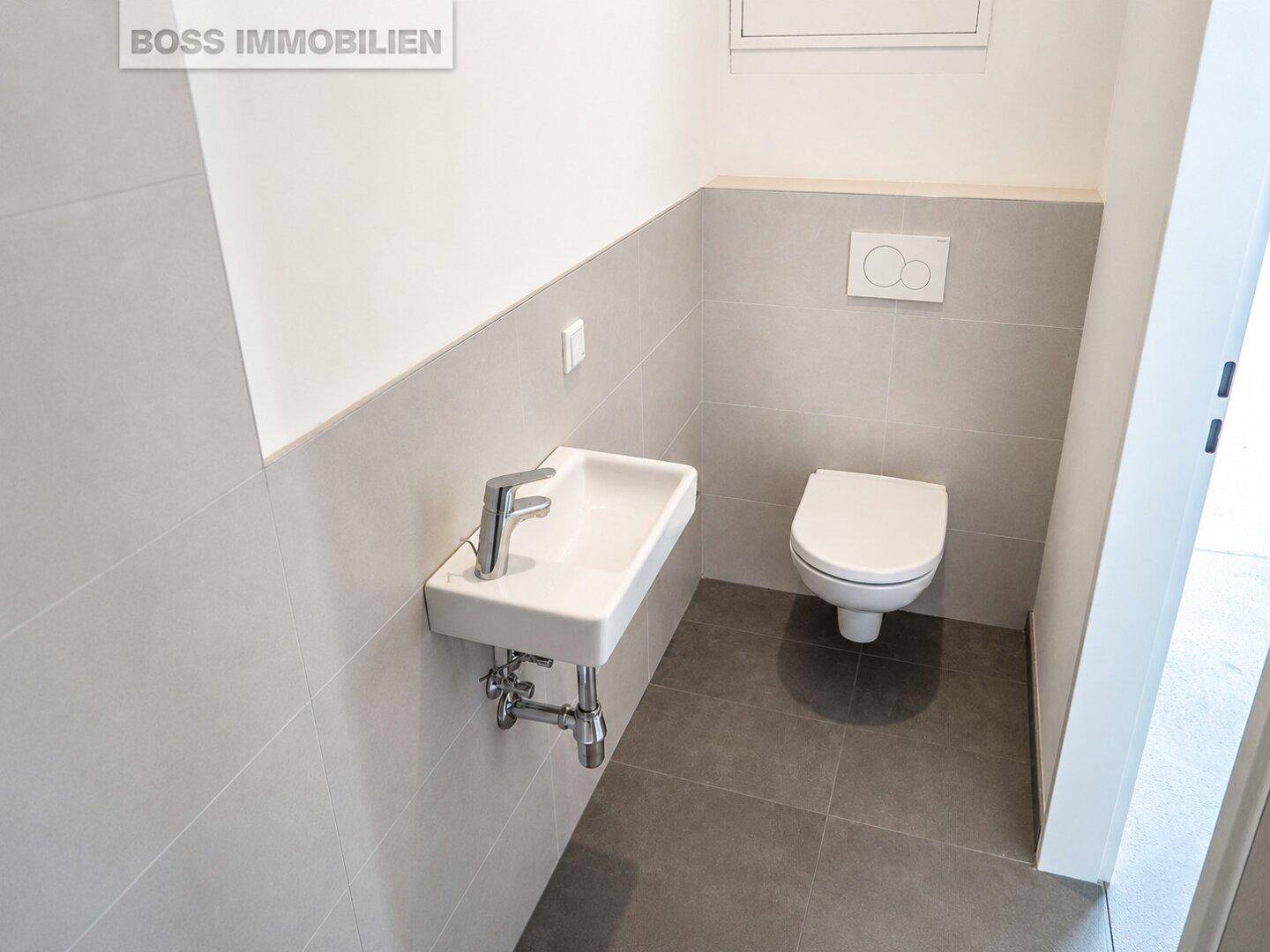 Modernes Gäste-WC mit wandhängendem WC und kleinem Waschbecken, ausgestattet mit grauen Fliesen.