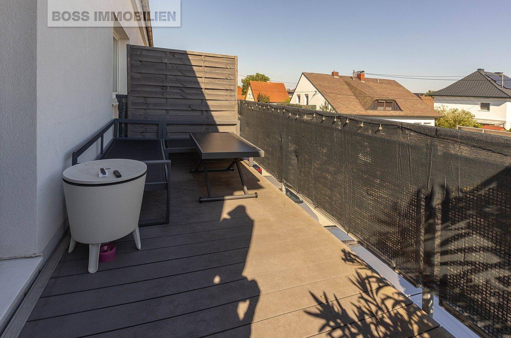 Sonniger Balkon mit Holzboden, Sitzgelegenheiten und Sichtschutz, ideal zum Entspannen.