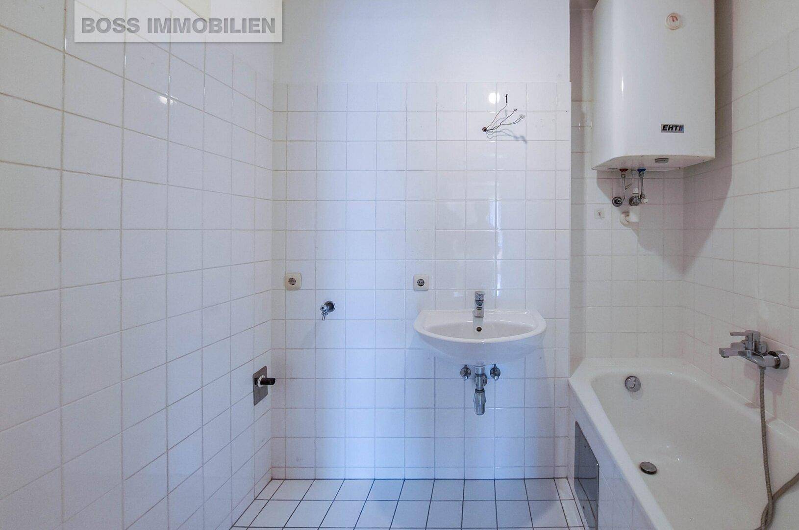 Badezimmer mit weißen Fliesen, Badewanne und Waschbecken, ausgestattet mit einem Warmwasserboiler.