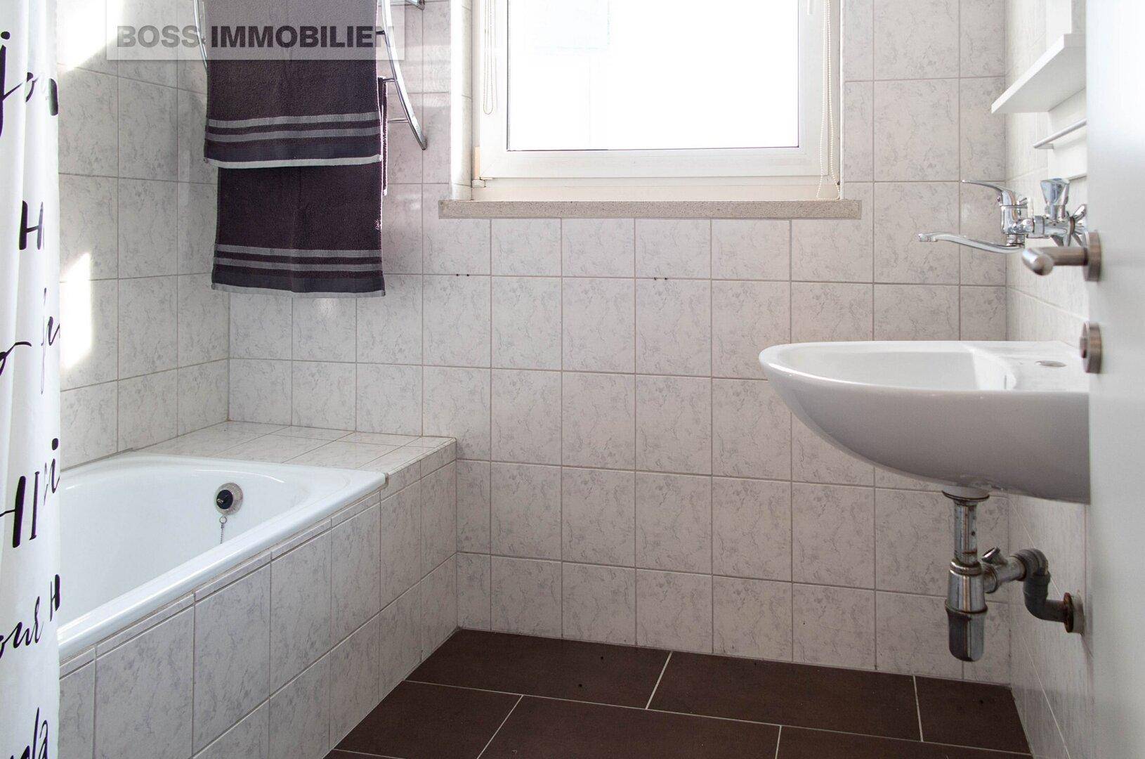 Badezimmer mit Badewanne, Waschbecken und Fenster, ausgestattet mit hellen Fliesen.