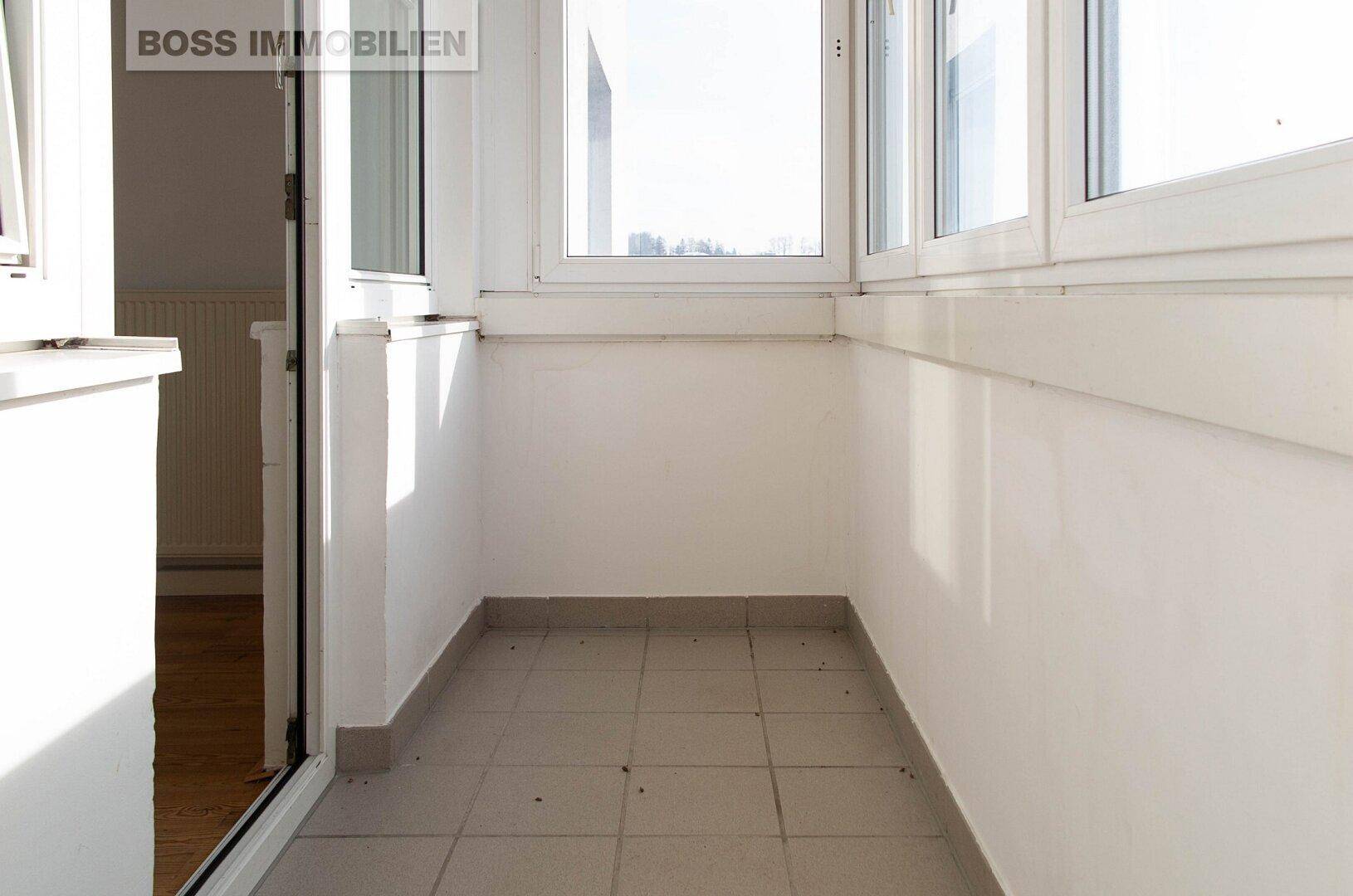 Heller, verglaster Balkon mit Fliesenboden und weitem Ausblick, ideal für alle Jahreszeiten.