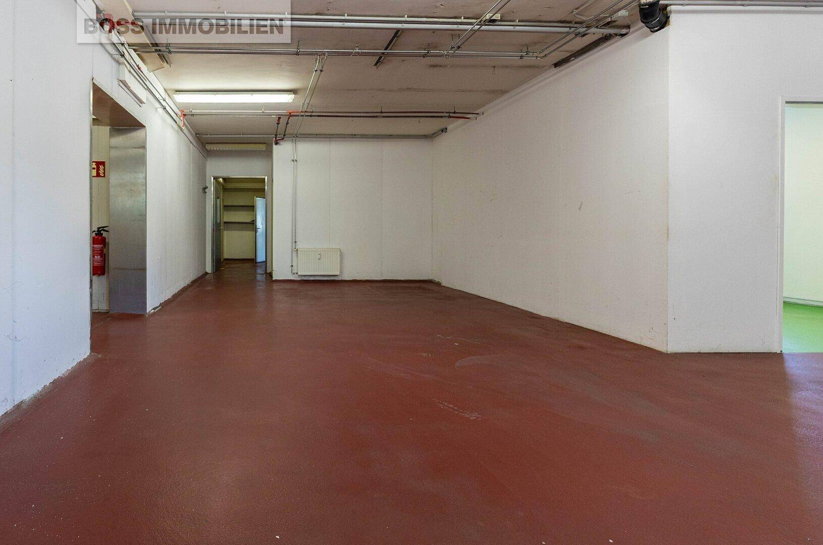Großer Lagerraum mit rotem Industrieboden, weißen Wänden und sichtbaren Leitungen an der Decke.