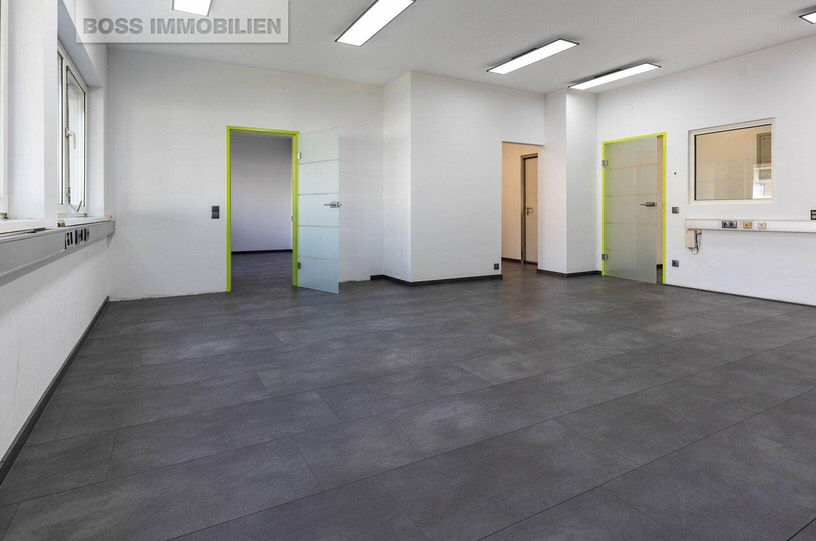 Geräumiger Büroraum mit dunklem Fliesenboden, weißen Wänden und mehreren Türen.