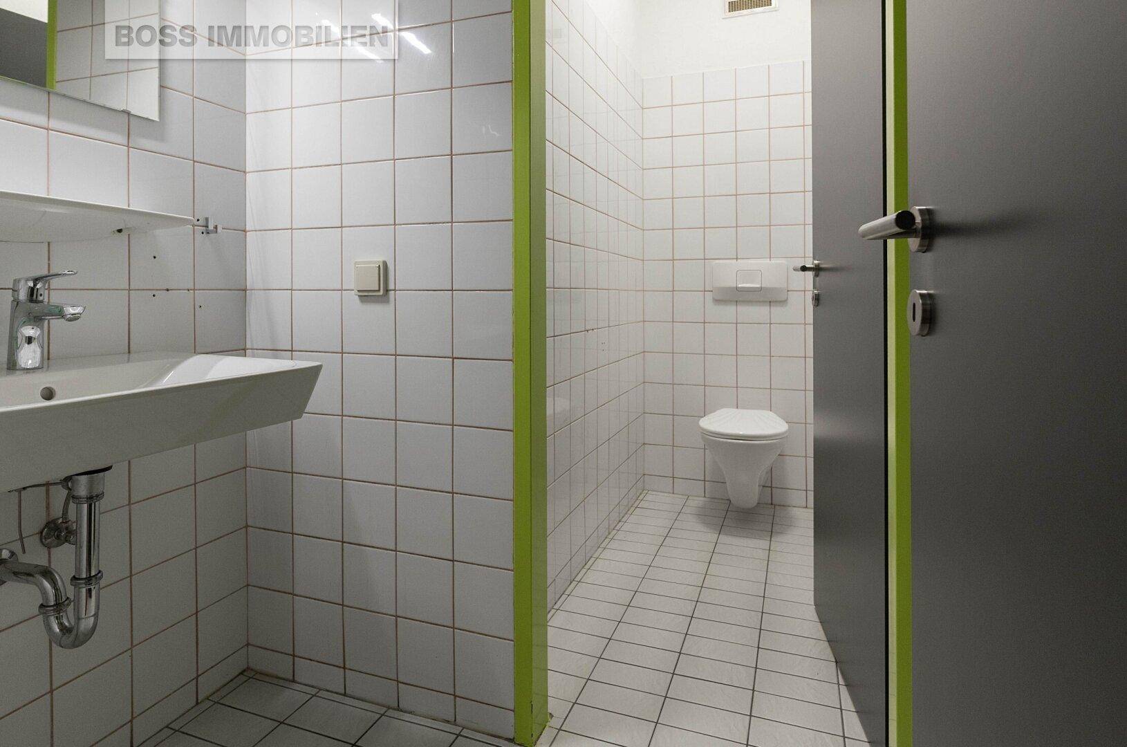 Saubere Toilette mit weißen Fliesen an Wänden und Boden sowie einem Waschbecken.