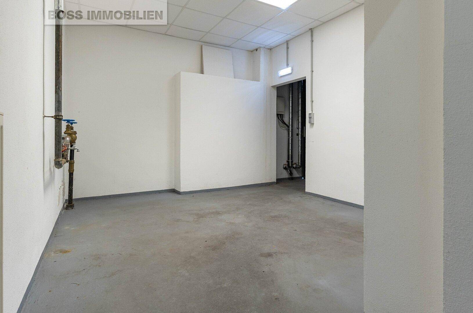 Nutzraum mit Betonboden, weißen Wänden und sichtbaren Installationen an der Wand.