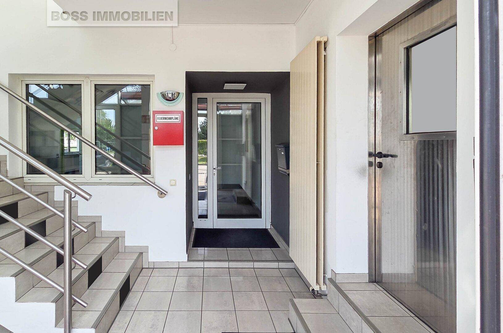 Eingangsbereich mit Treppe, Fliesenboden und einer Glastür zum Gebäudeinneren.