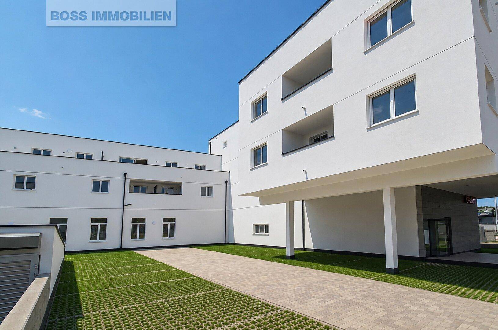 Gepflegte Grünfläche mit Rasen und befestigtem Weg neben dem modernen Wohngebäude.