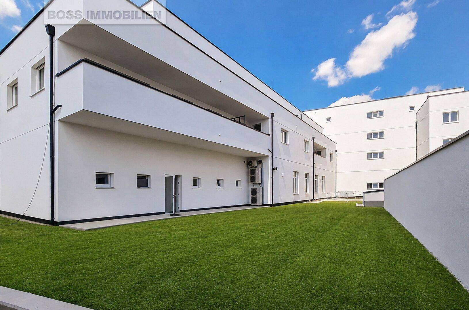 Große Rasenfläche und Balkone an der Seite des modernen Wohngebäudes unter blauem Himmel.