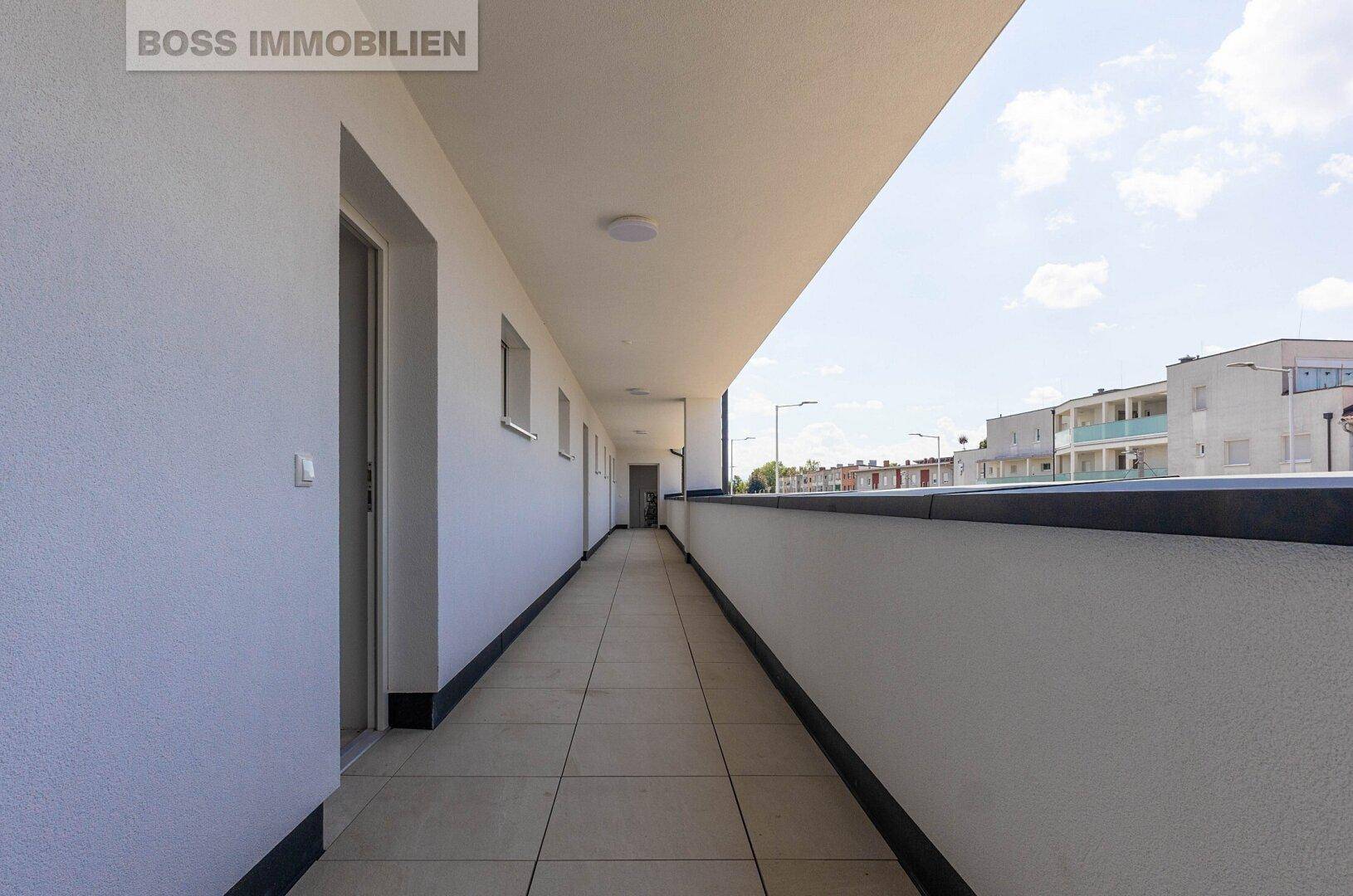 Langer, gefliester Balkon mit weißer Brüstung und Blick auf die Umgebung.