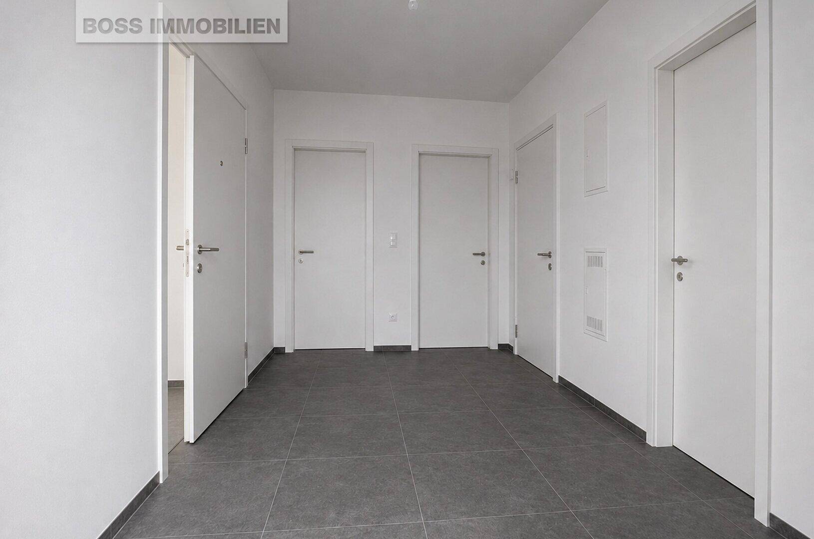 Moderner Flur mit dunklen Fliesen und mehreren weißen Türen zu den Zimmern.