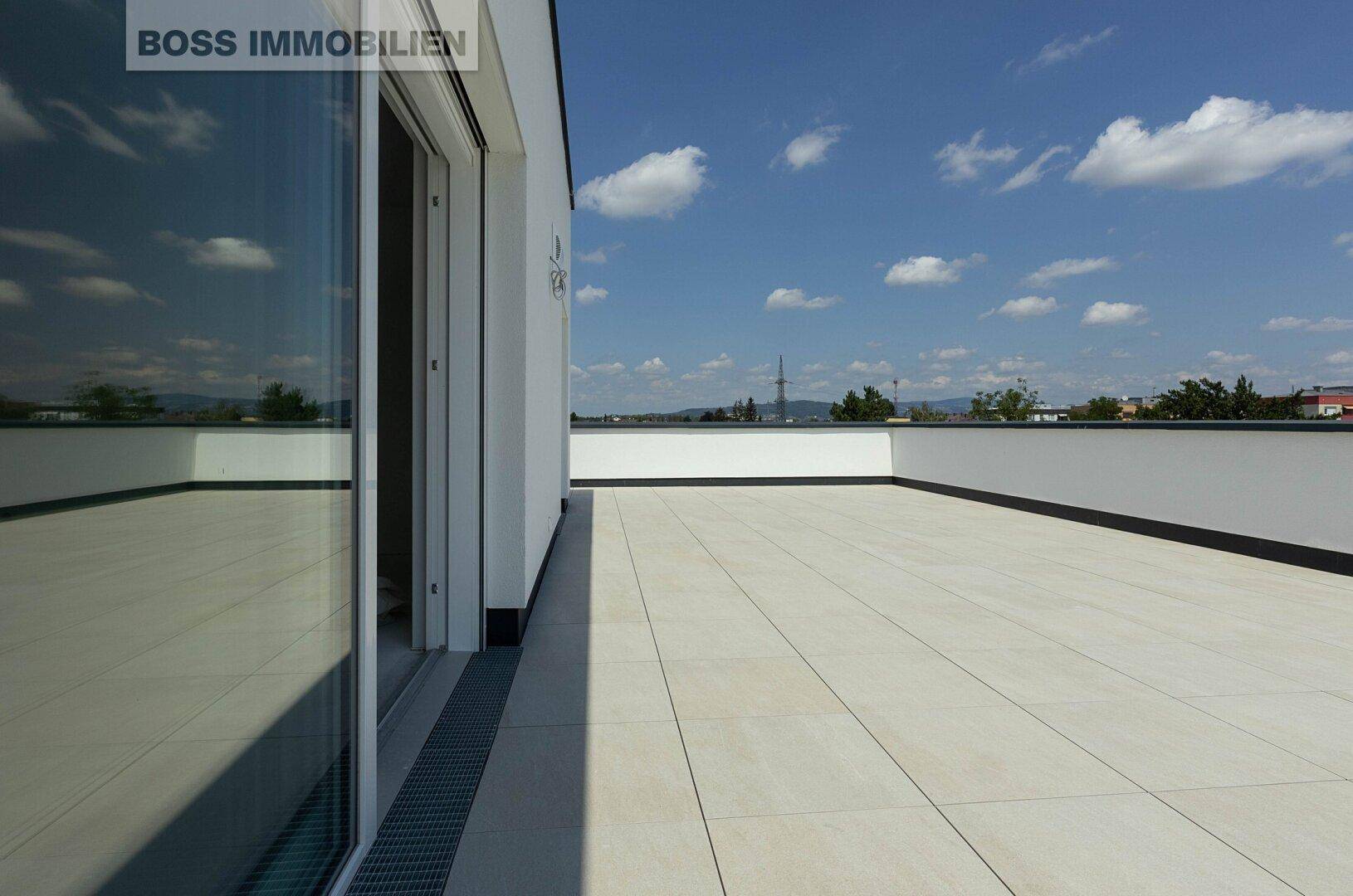 Weitläufige, leere Dachterrasse mit hellen Fliesen und Zugang zum Innenbereich.