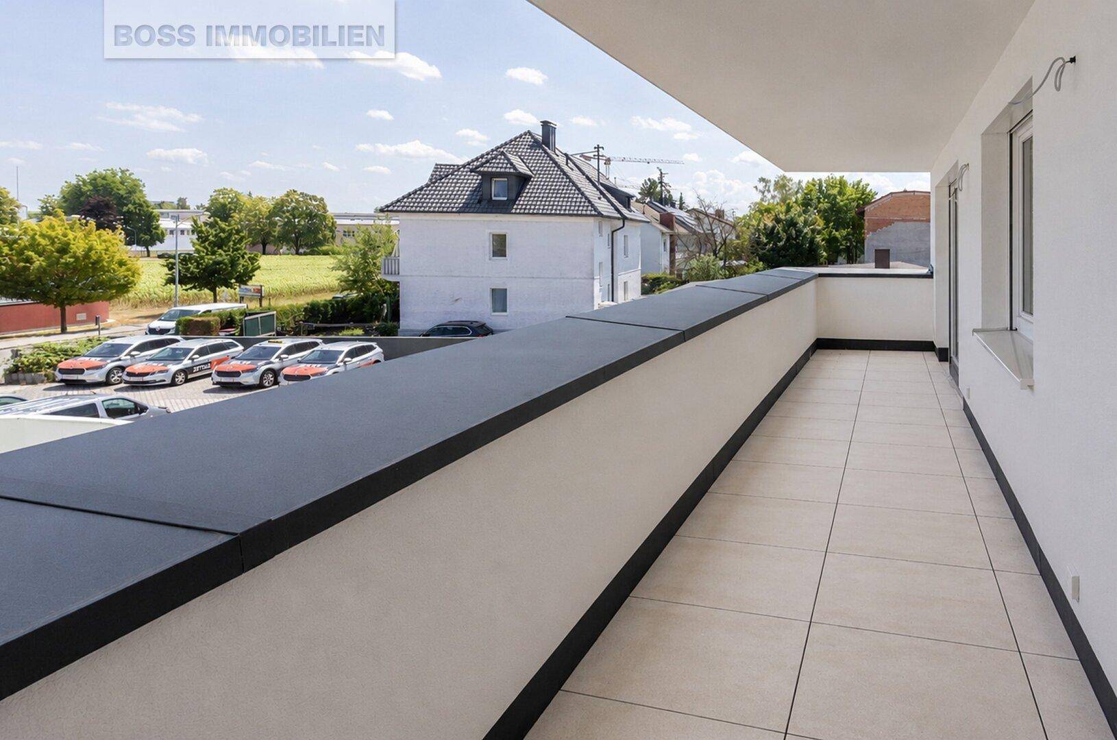 Langer Balkon mit Fliesenboden und Blick auf die Umgebung und geparkte Autos.