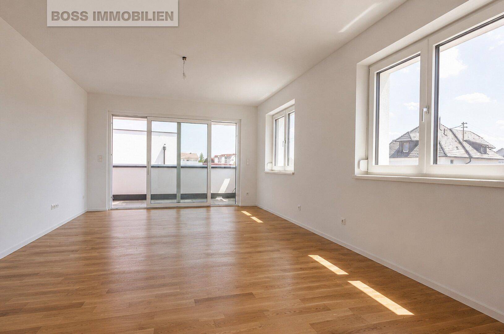 Heller, leerer Wohnraum mit Holzboden, großen Fenstern und Zugang zu einem Balkon.
