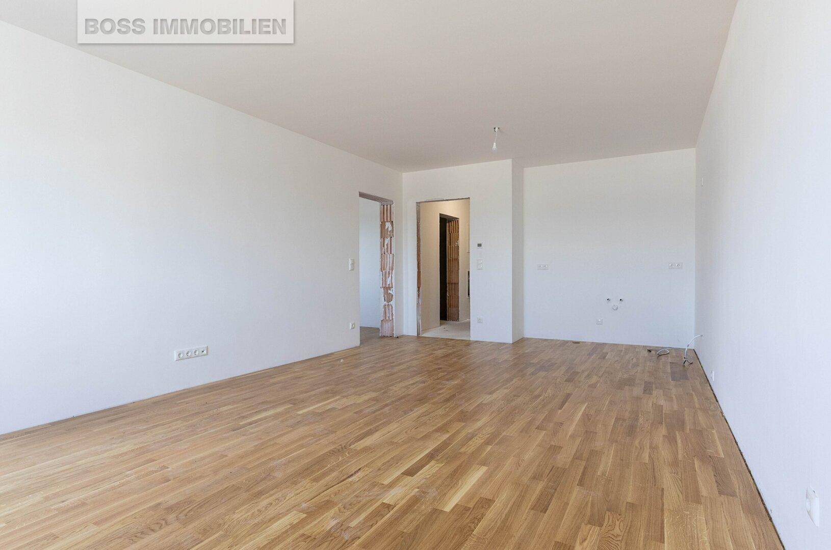 Geräumiger, leerer Raum mit Holzboden und Zugang zu weiteren Zimmern.