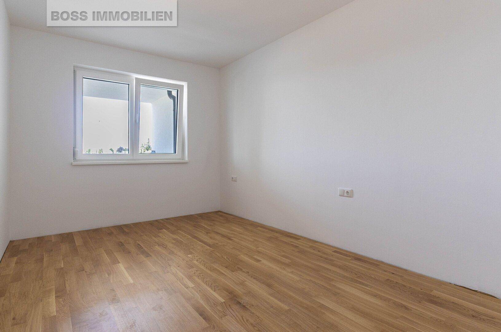 Helles, leeres Zimmer mit Holzboden und einem Fenster, ideal als Schlaf- oder Arbeitszimmer.