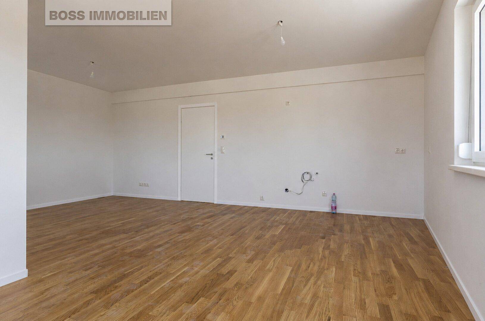 Leerer Raum mit Holzboden, weißen Wänden und einer Tür, bereit zur individuellen Gestaltung.