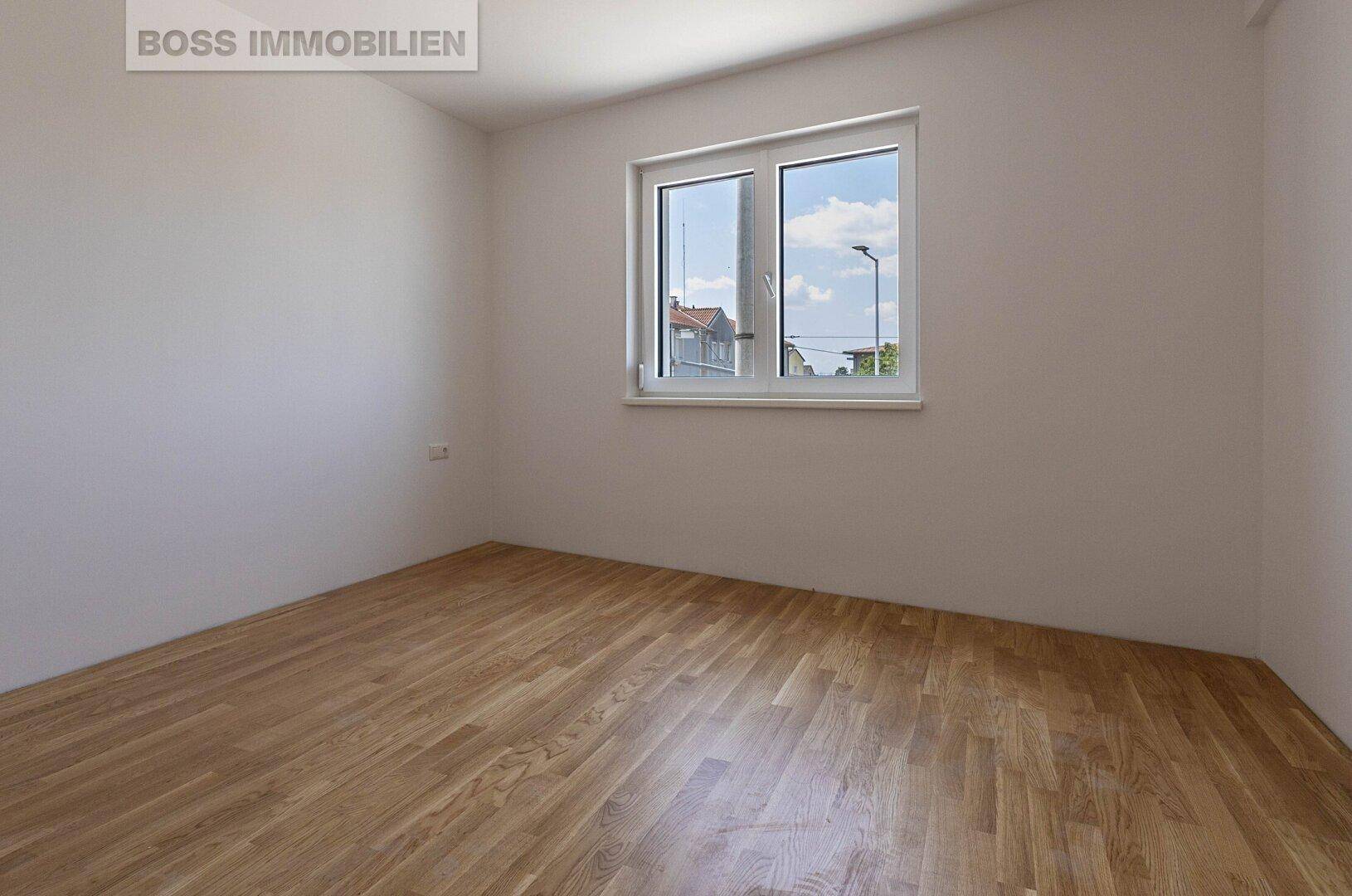Helles, leeres Schlafzimmer mit Holzboden und einem Fenster, das einen Blick nach draußen bietet.