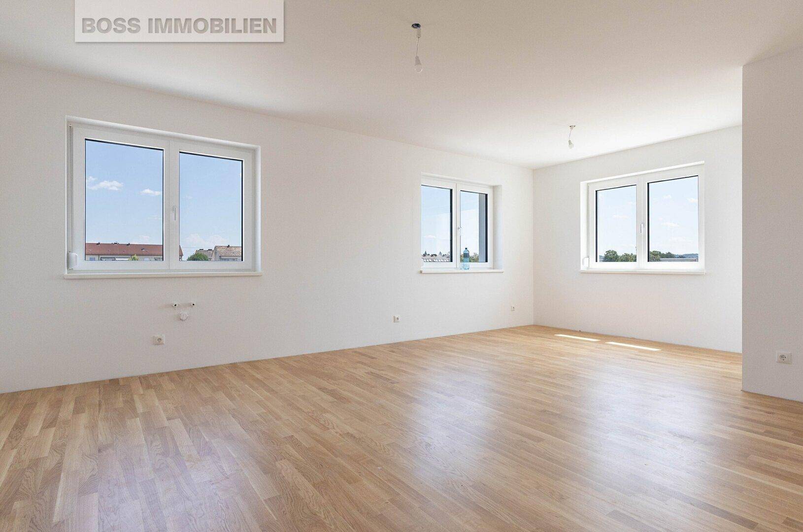 Heller, leerer Raum mit großen Fenstern und neuem Holzfußboden, ideal als Wohnbereich.