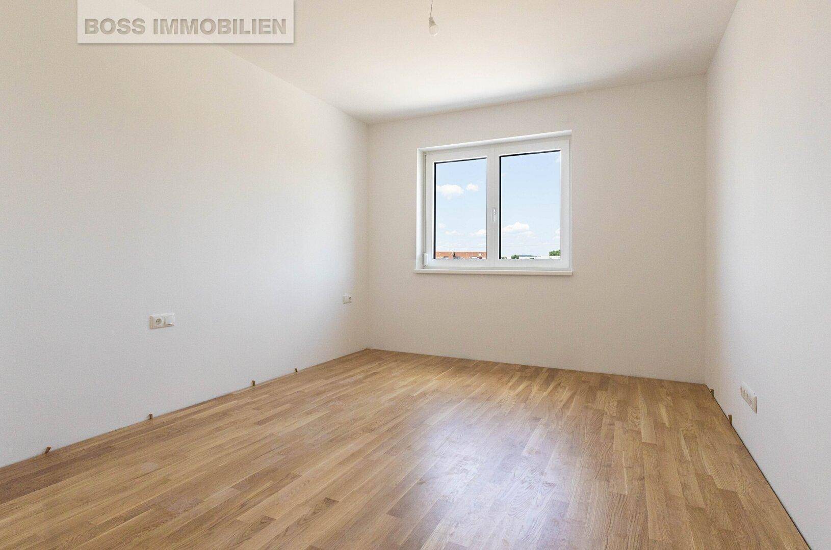 Helles, leeres Schlafzimmer mit Holzboden und einem Fenster, das den Raum mit Licht füllt.